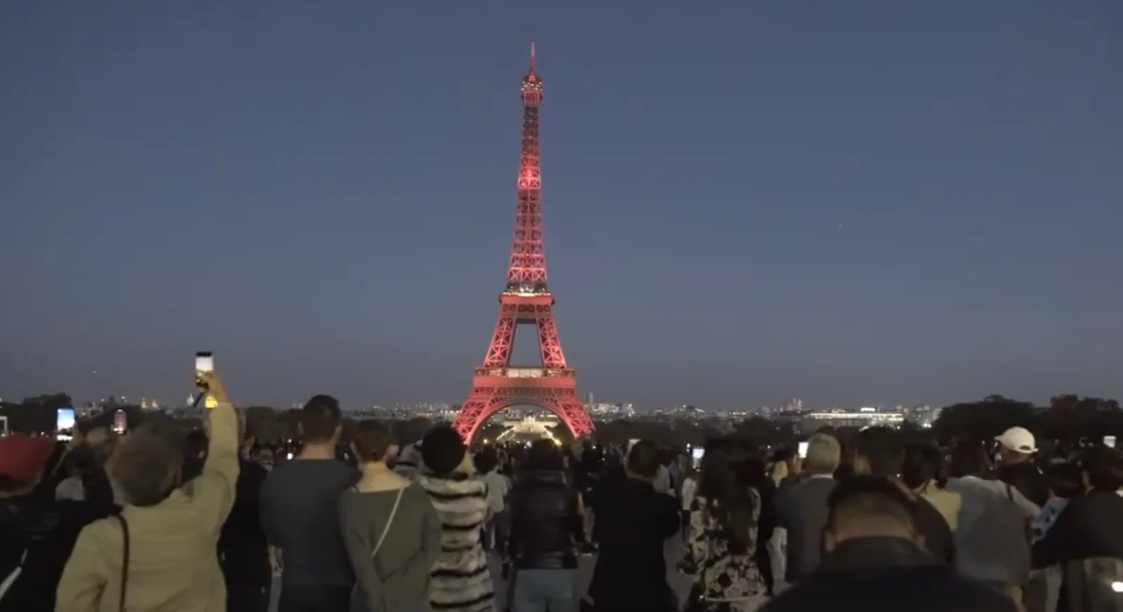 A crowd at the Trocadéro watching the Eiffel Tower lit red.