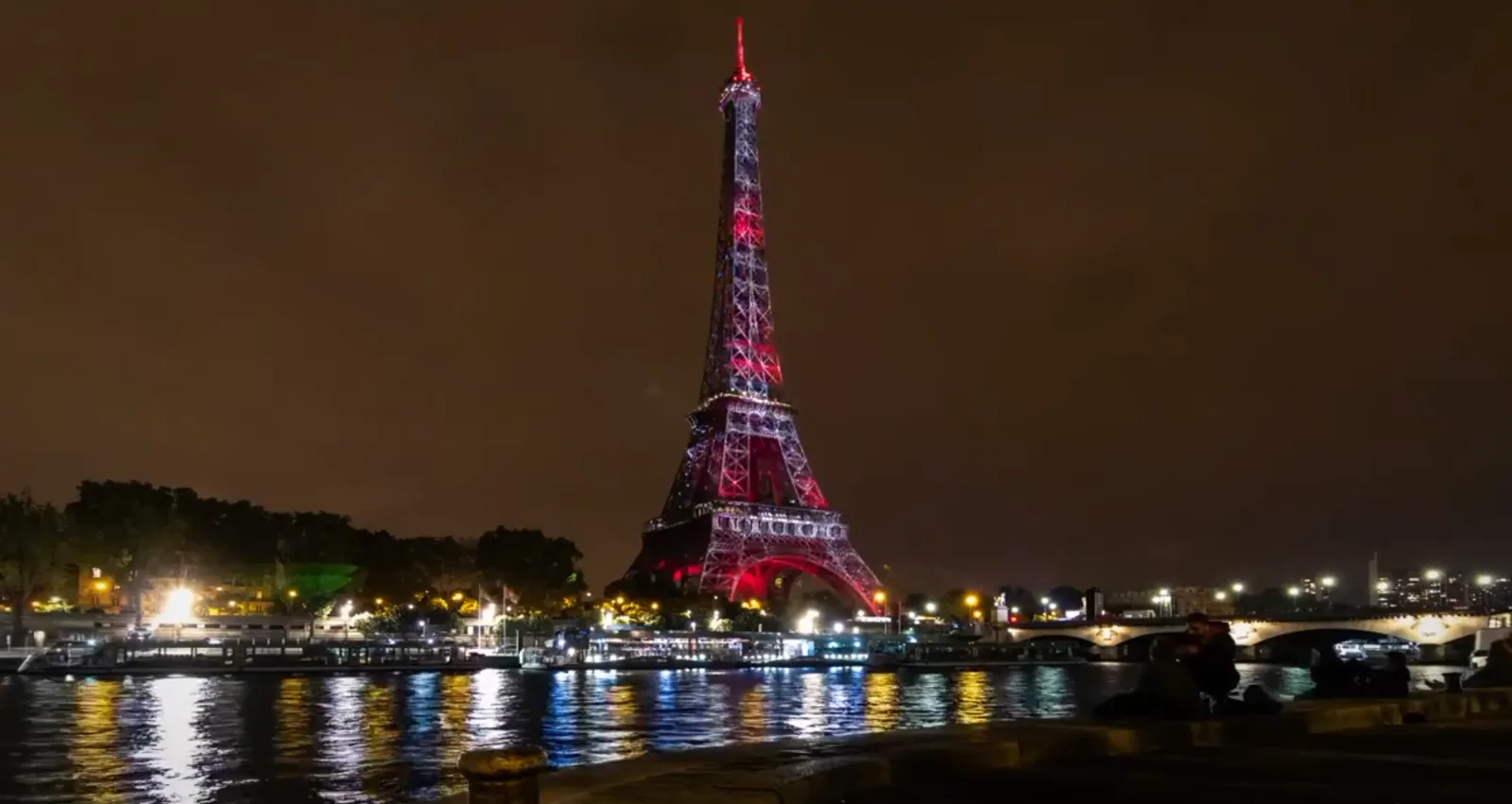 The Eiffel Tower carrying a red and white light show, seen across the Seine.