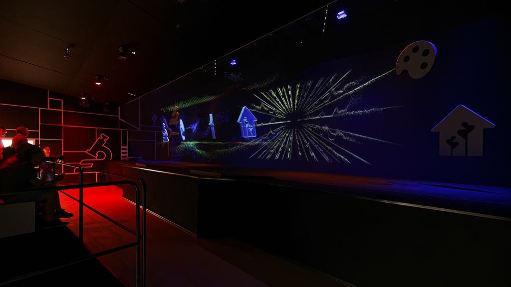 The audience seated in red light as the main show bursts across the layered screens, the icons of Dutch invention glowing from the dark walls
