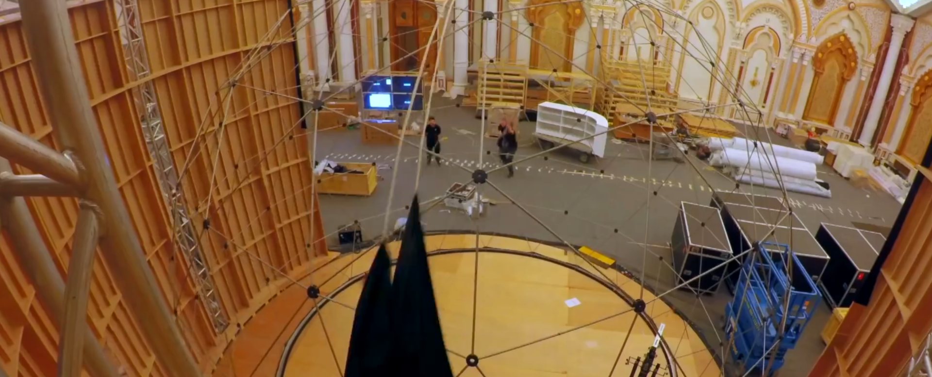 A geodesic dome frame being skinned inside an ornate hall
