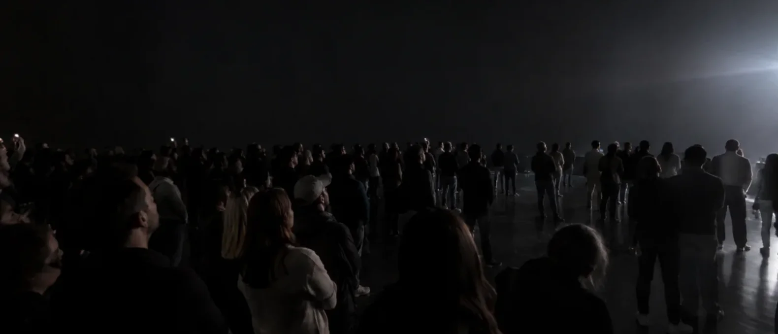 An audience in a dark hall turned together toward one bright moment.