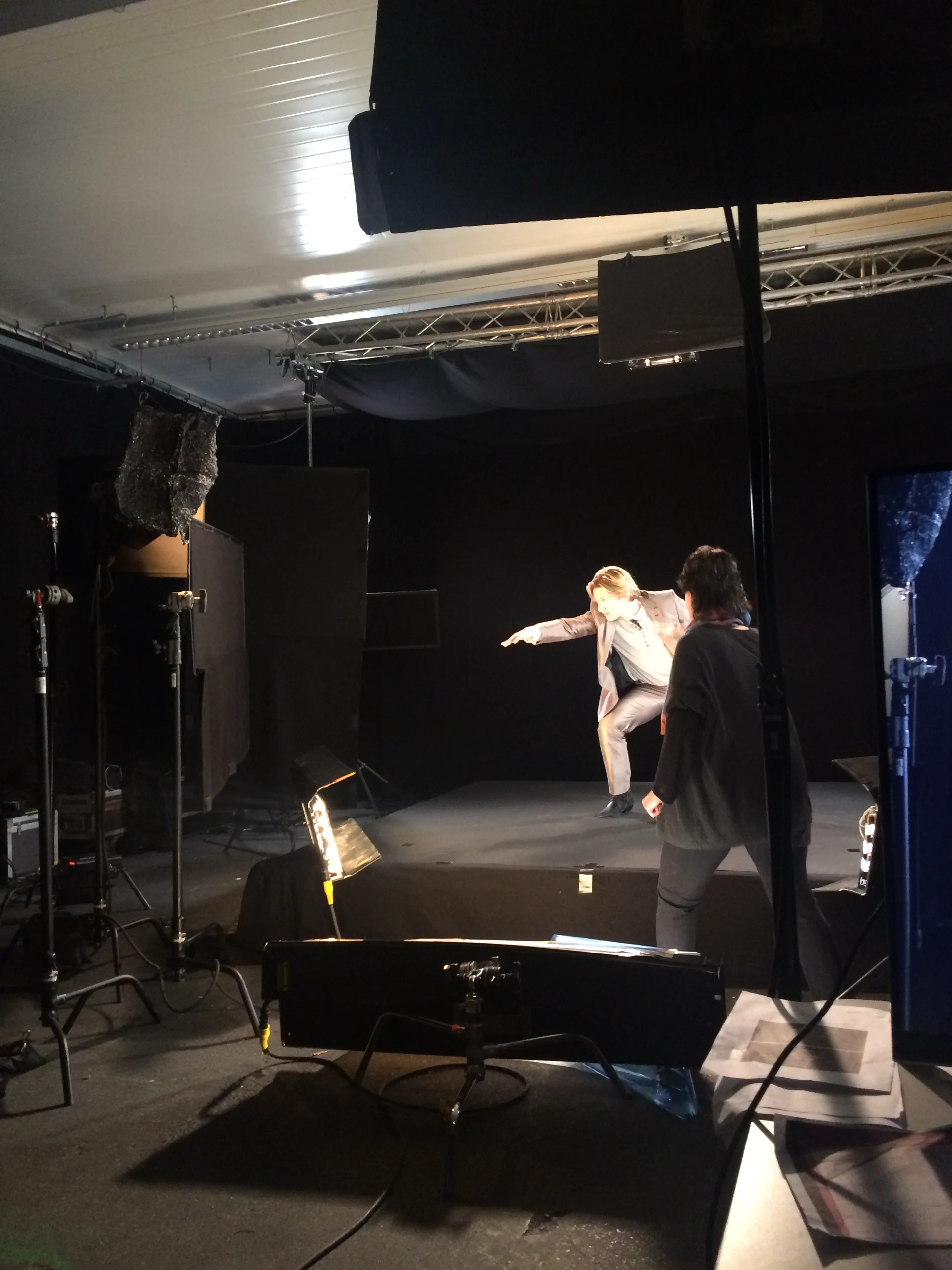 The capture stage: a performer mid-move on a black riser in a black-void studio, soft light banks around him, the director beside camera