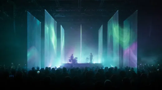 A concert stage with eight transparent screens in depth, carrying an aurora of teal light over the crowd.