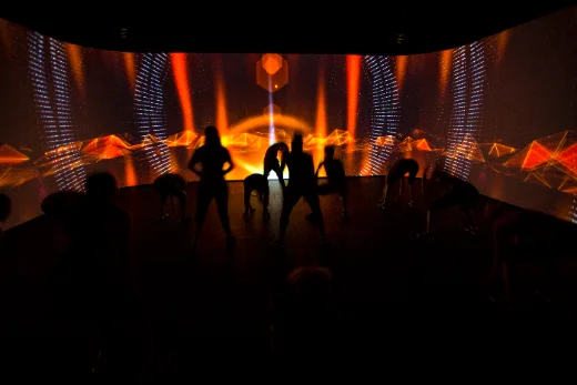 A fitness class facing a projected horizon in a darkened studio.